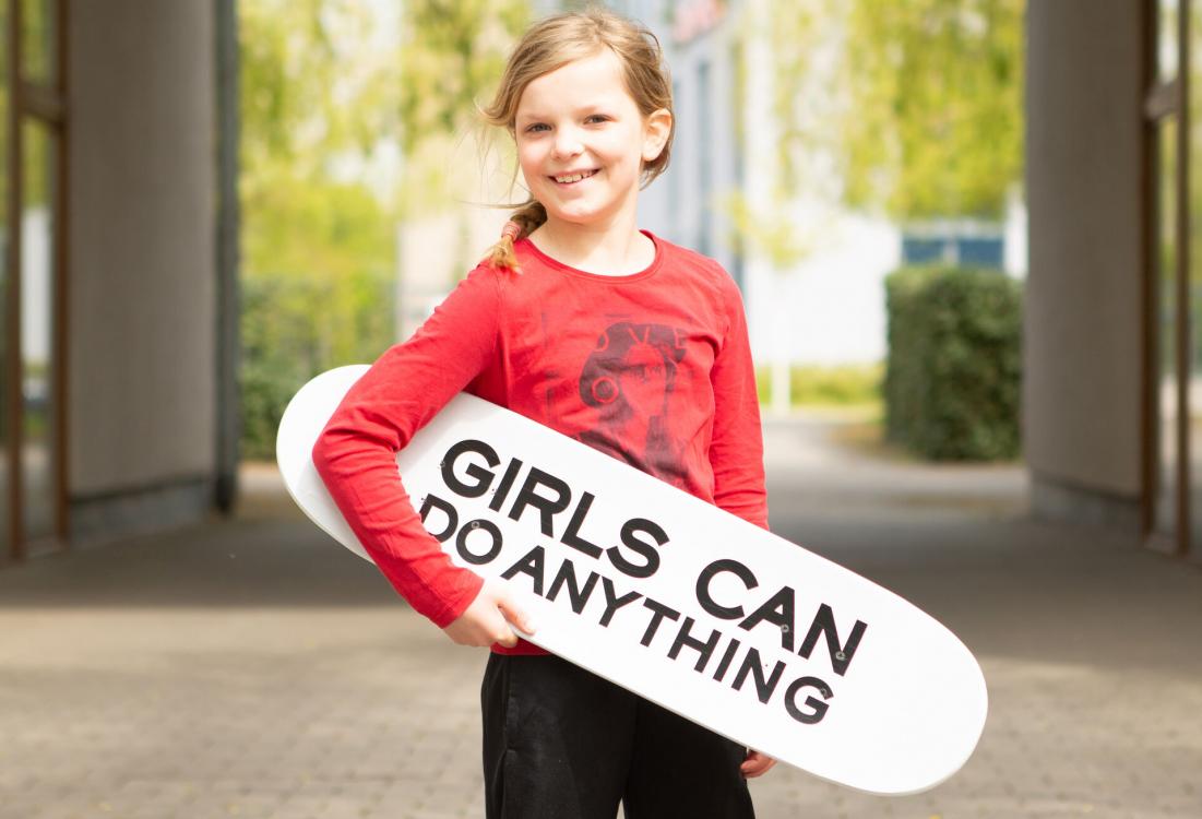 Mädchen mit roten Shirt und Skateboard im Arm.