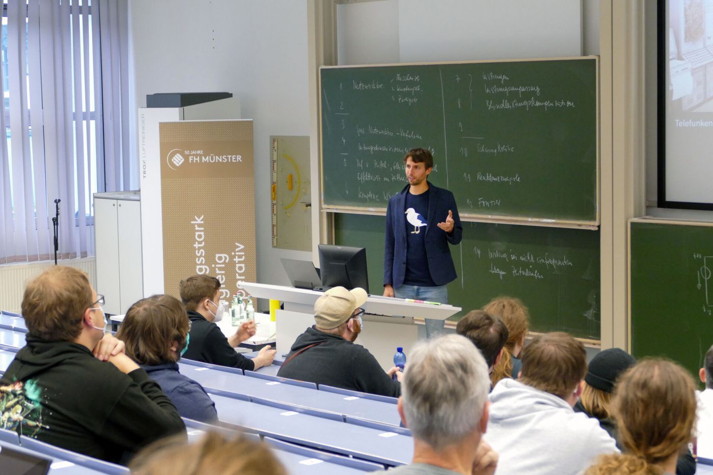 Dr. Sven Köppel steht in einem Hörsaal und spricht zum Publikum.  (Foto: FH Münster/Jana Schiller)