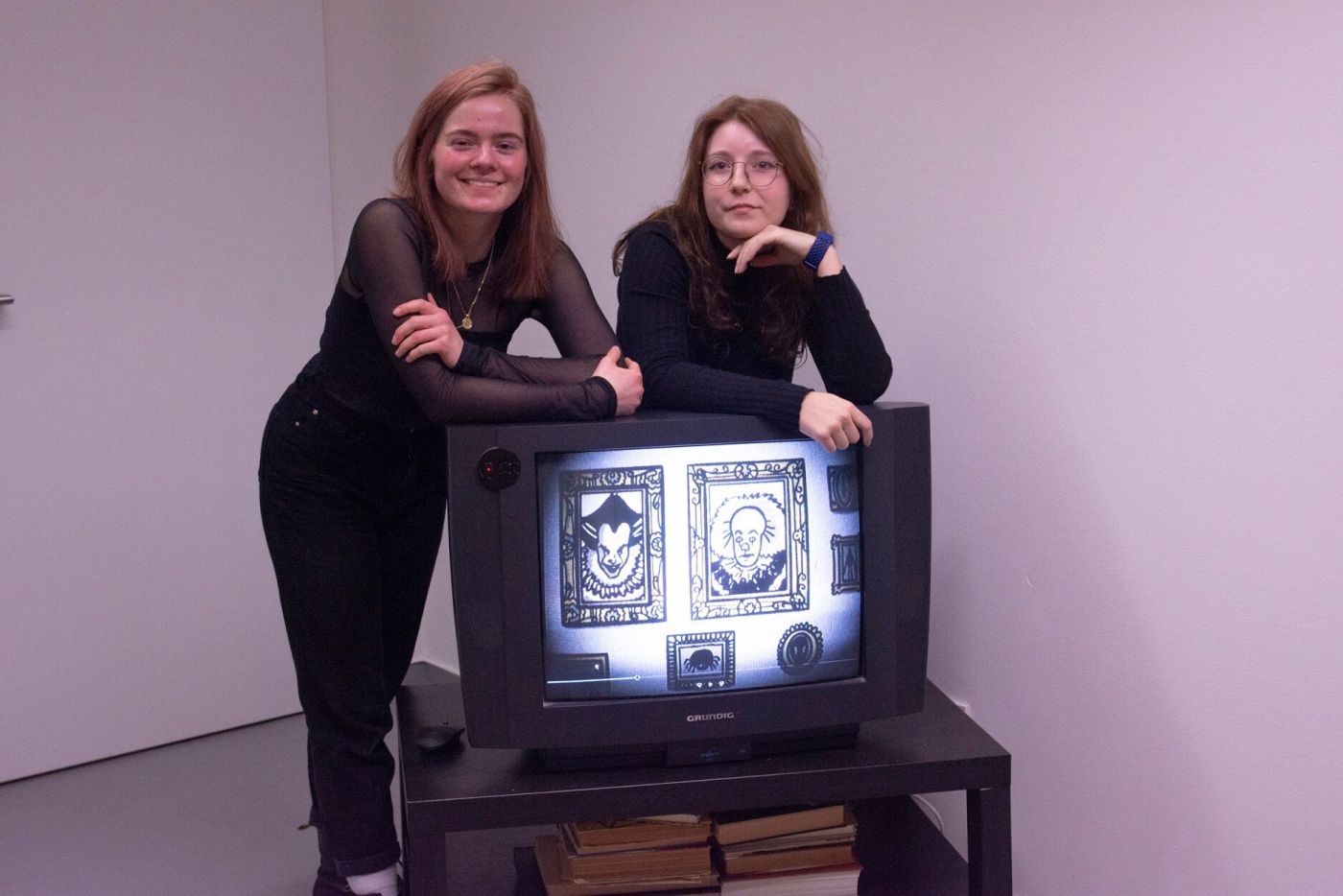Zwei Frauen posieren an einem Fernseher, auf dem ein Animationsfilm gezeigt wird. 