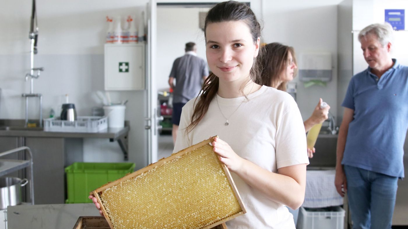 Eine junge Frau hält eine Honigwabe in der Hand.