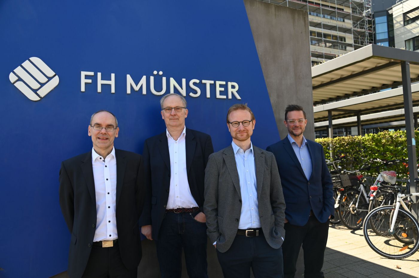 Vier Männer, der Deakan des Fachbereichs Wirtschaft der FH Münster sowie drei Studiengangsleiter des Fachbereichs, stehen vor dem FH-Münster-Schild am Fachhochschulzentrum.