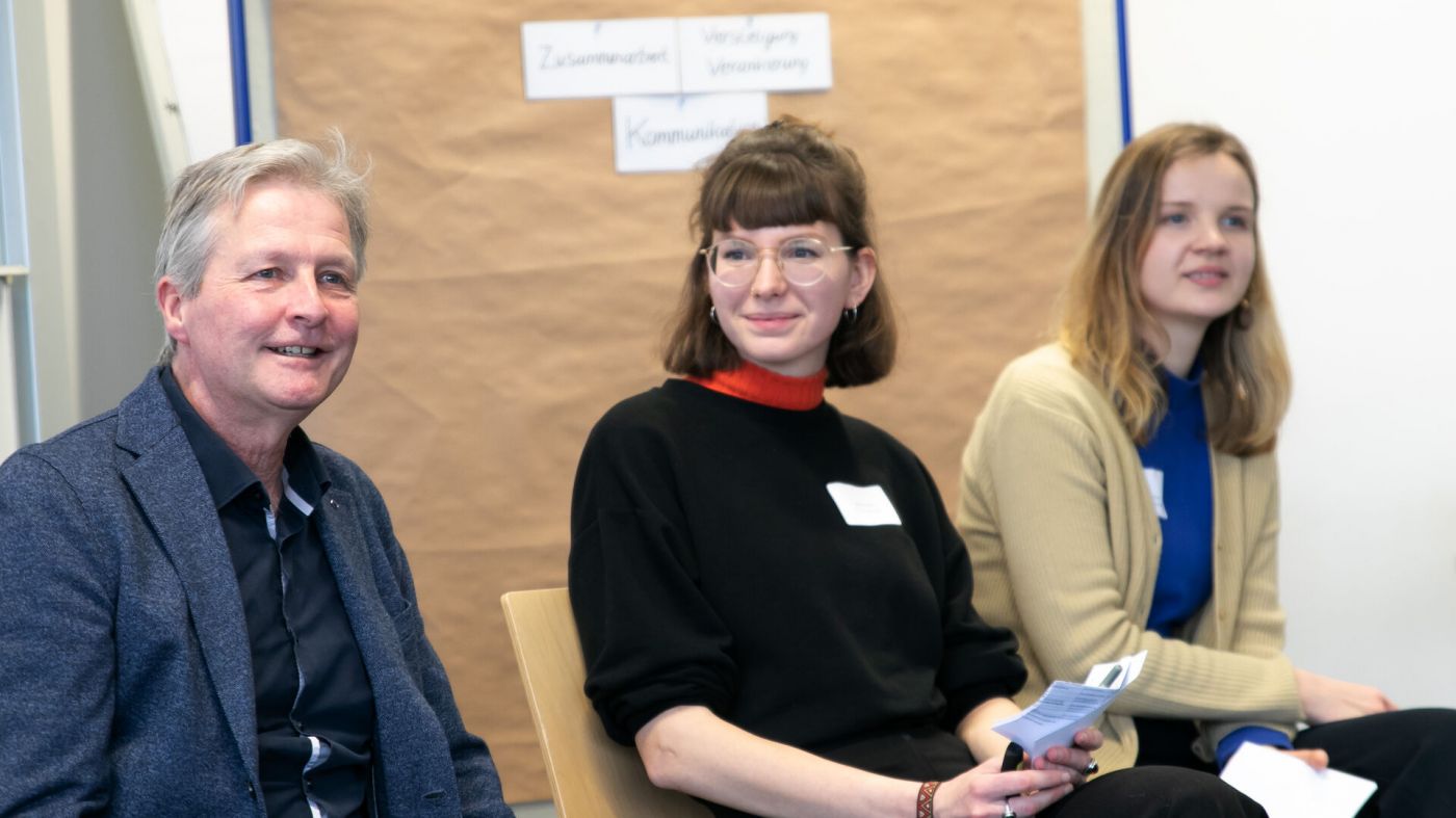 Ein Mann und zwei Frauen sitzen nebeneinander in einem Seminarraum der FH Münster.