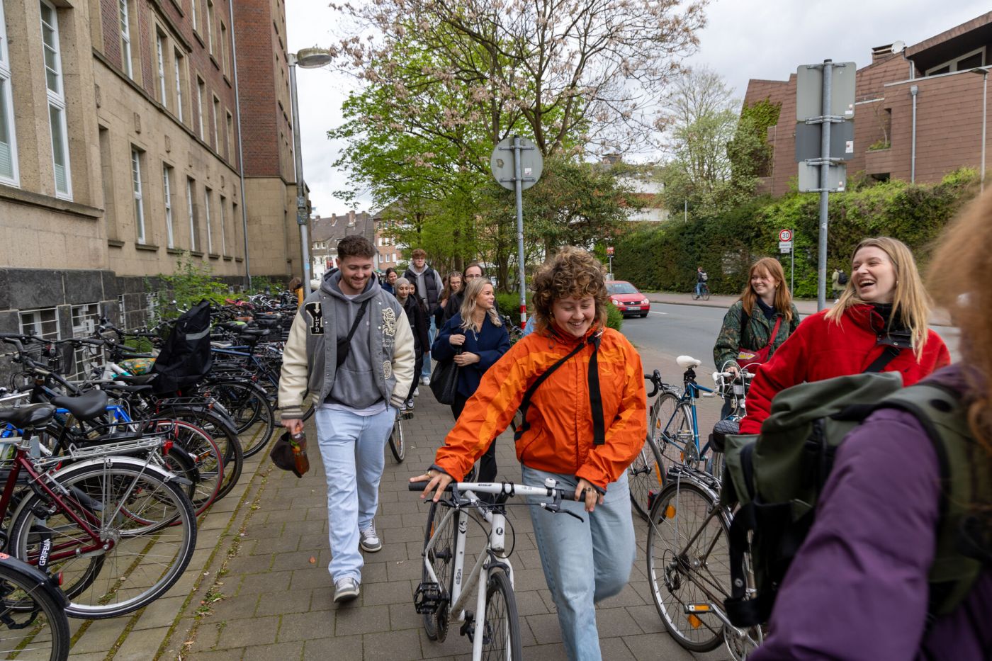 Eine Gruppe von Personen geht an einem Gebäude vorbei, mehrere Personen schieben Fahrräder und lachen. (Foto: FH Münster/Anna Thelen)