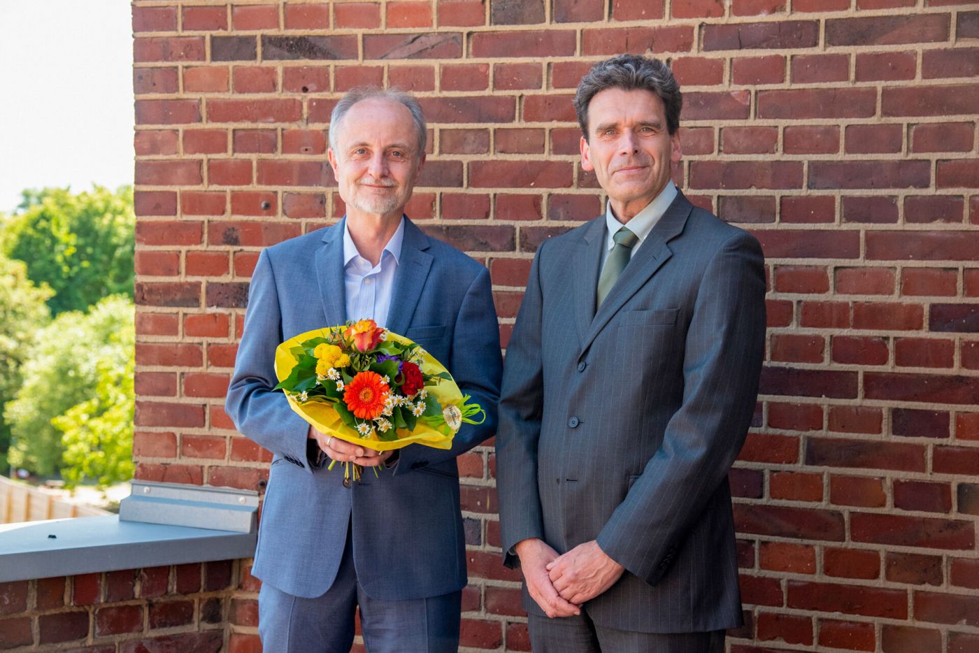 Zwei Männer stehen nebeneinander, einer hält einen Blumenstrauß. (Foto: FH Münster/Michelle Liedtke)