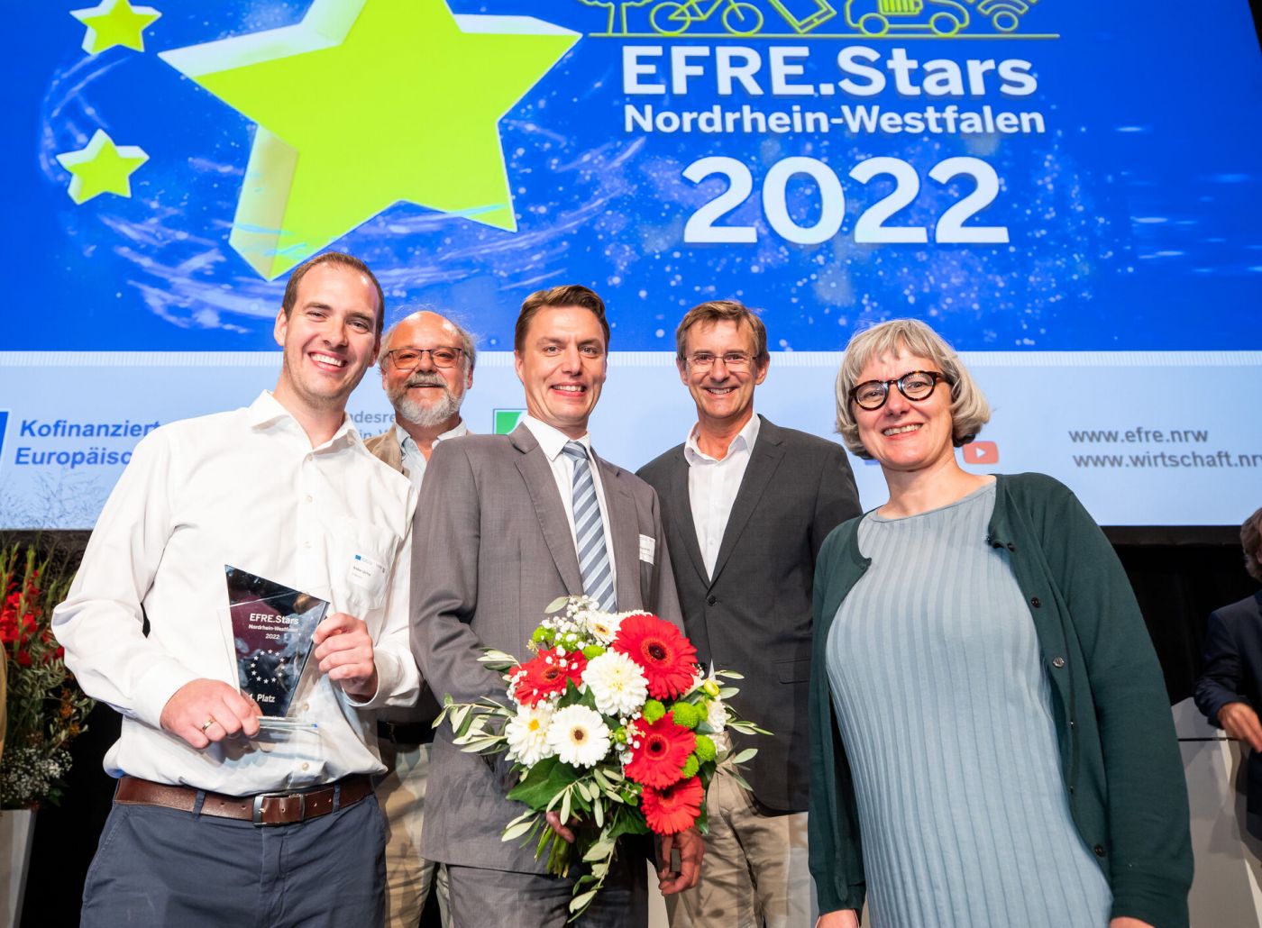 Die Preisträger des EFRE.Stars 2022 halten einen Blumenstrauß und eine Trophäe in der Hand.  (Foto: Udo Geisler)