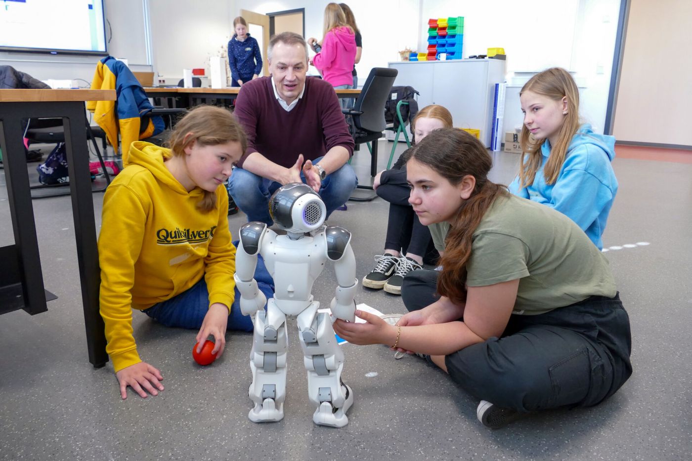 Schülerinnen sitzen auf dem Boden und sprechen mit einem kleinen Roboter. (Foto: FH Münster/Jana Bade)