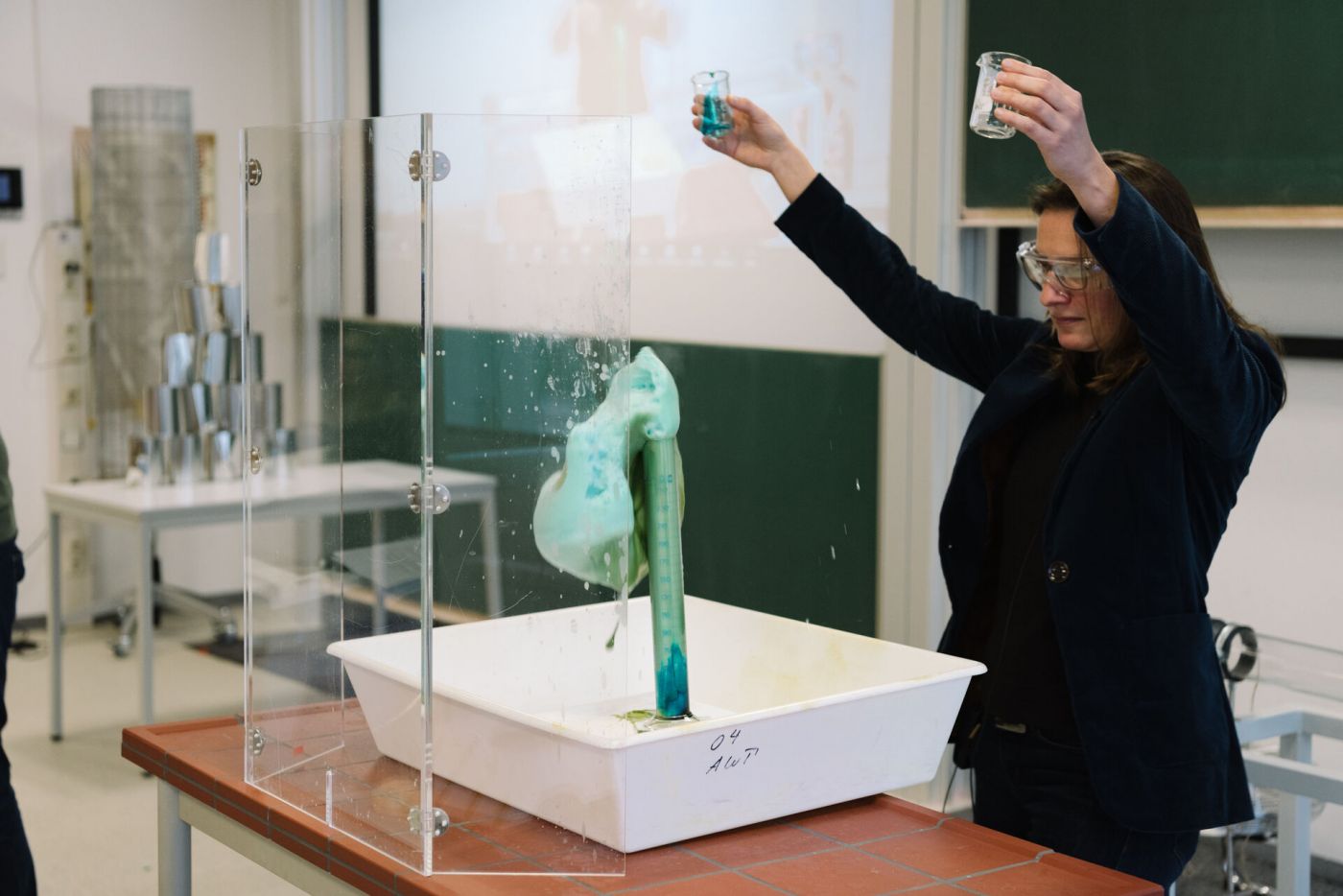Eine Professorin führt ein Experiment durch. Dabei quillt grüne Paste aus einem Reagenzglas hervor.