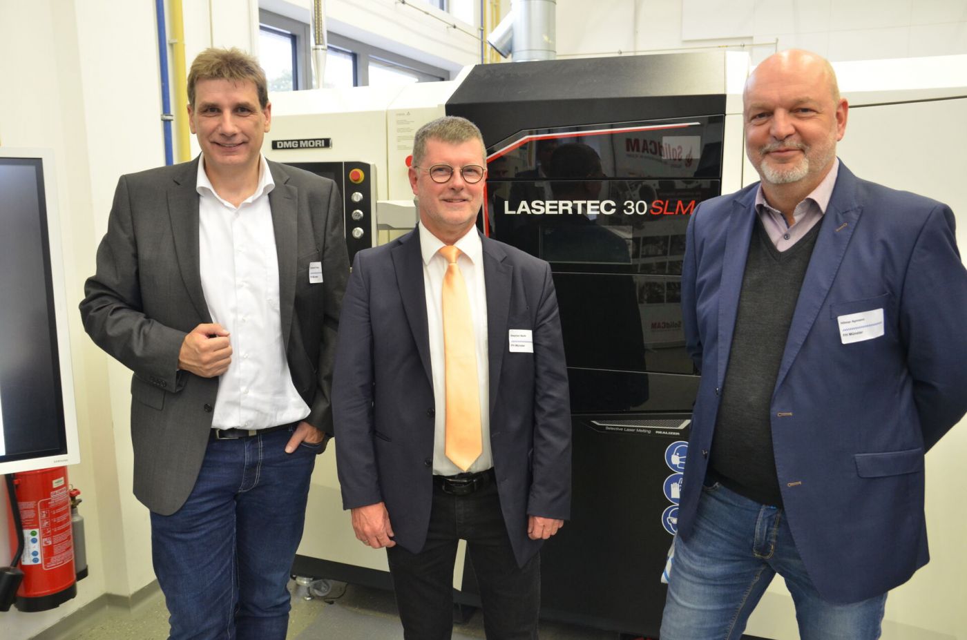 Drei Männer stehen vor einem Metall-3D-Drucker. 