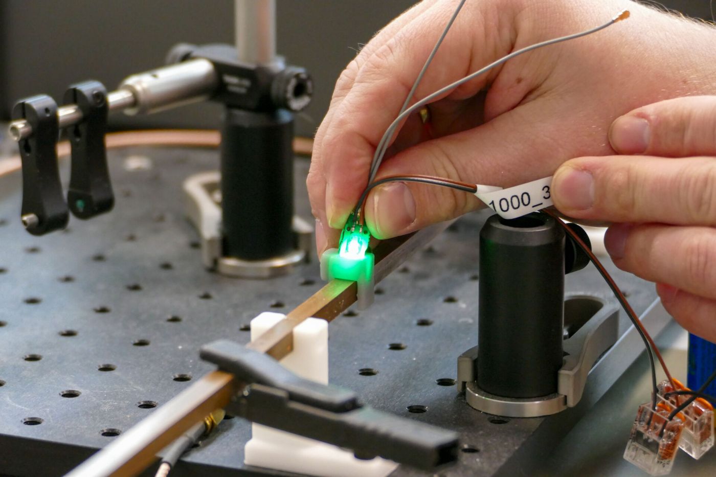 Eine Hand hält ein kleines, grün leuchtendes elektronisches Gerät in einen Versuchsaufbau. (Foto: FH Münster/Jana Bade)