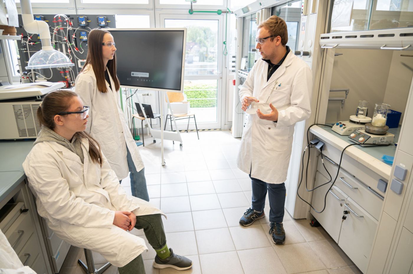 Zwei Schülerinnen und ein Student unterhalten sich im Labor.