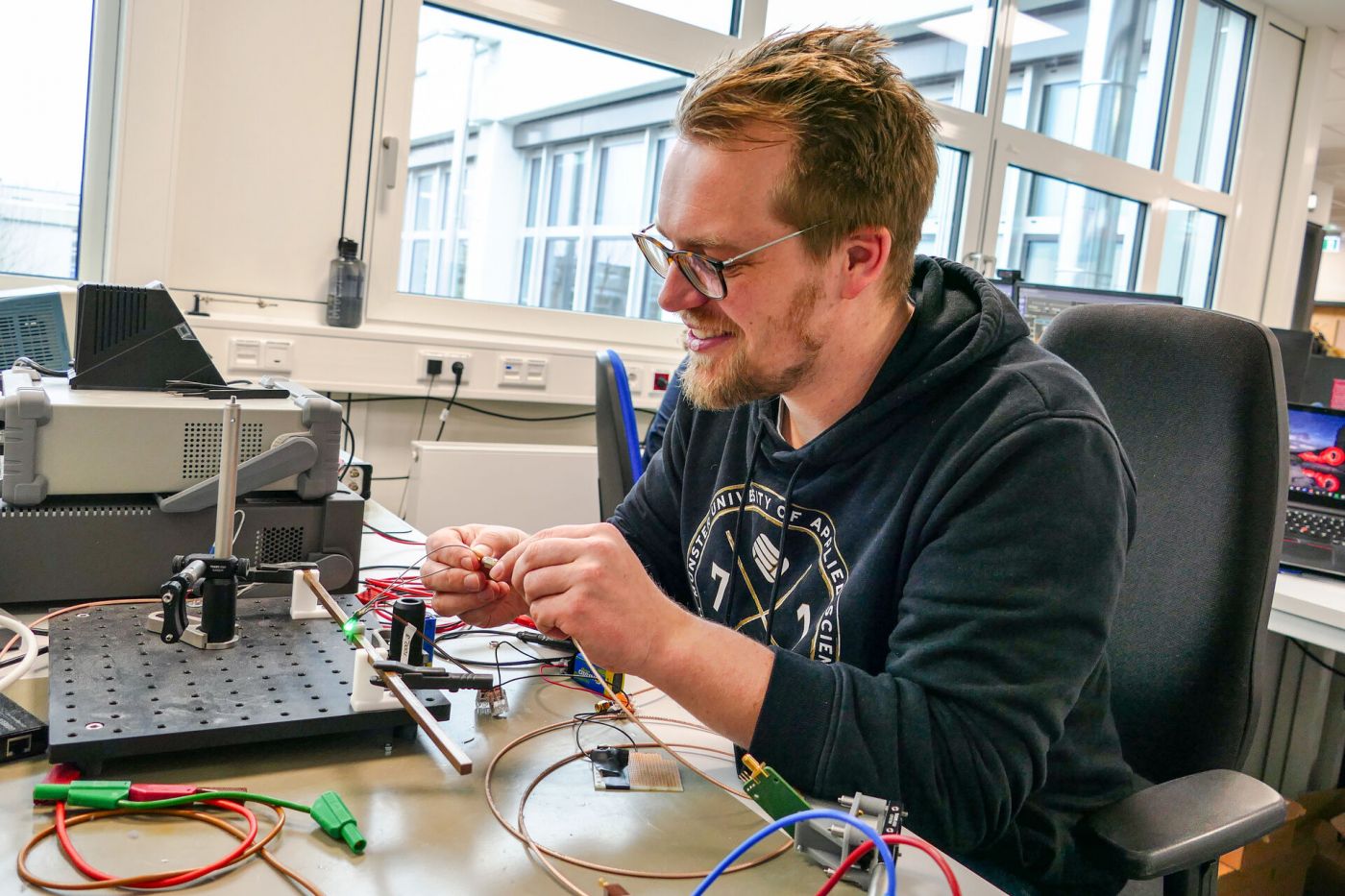 Eine Person arbeitet in einem Labor mit einem kleinen, grün leuchtenden elektronischen Gerät. (Foto: FH Münster/Jana Bade)