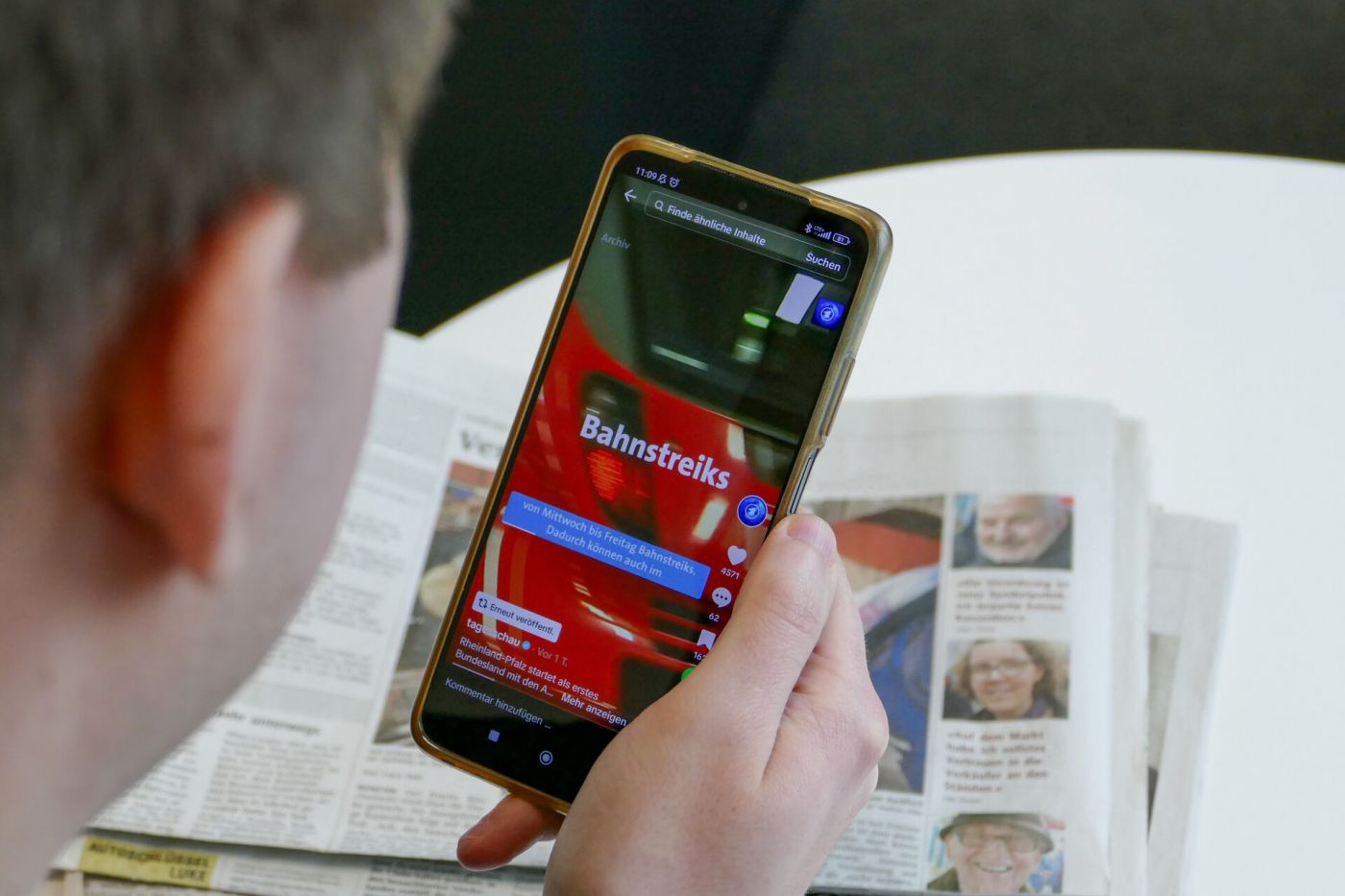 Eine Person sieht sich Nachrichten auf dem Smartphone an. Im Hintergrund liegen Zeitungen.  (Foto: Foto: FH Münster/Jana Bade)