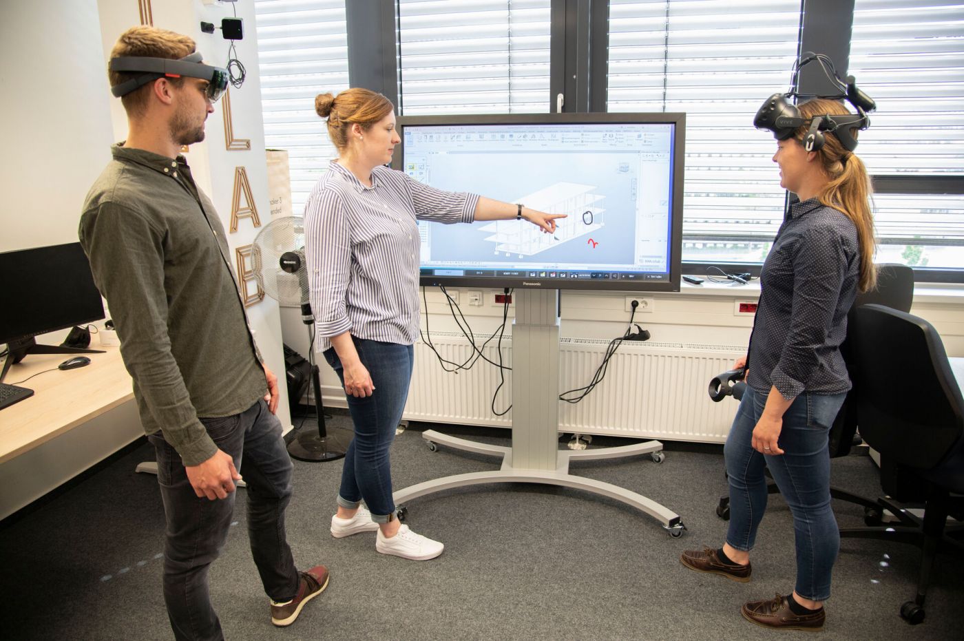 Ein Mann und zwei Frauen arbeiten an einem Bildschirm. Sie tragen Virtual Reality Brillen. 