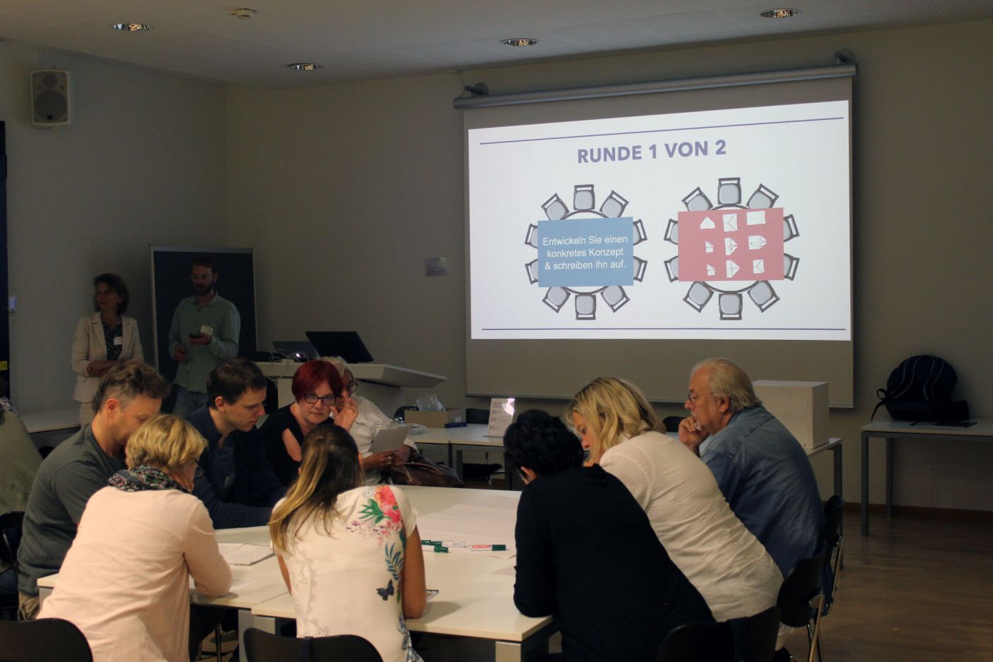 Teilnehmer*innen eines Workshops sitzen an einem Tisch, im Hintergrund ist eine Präsentation zu sehen. (Foto: FH Münster/Tjorven Thorwesten )