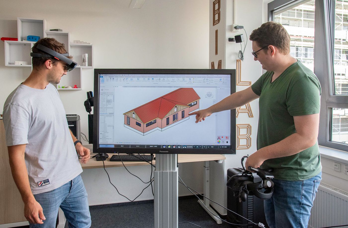 Zwei Männer halten Virtual-Reality-Brillen und stehen vor einem Bildschirm, das ein digitales gebäudemodell zeigt. (Foto: FH Münster/Michelle Liedtke)