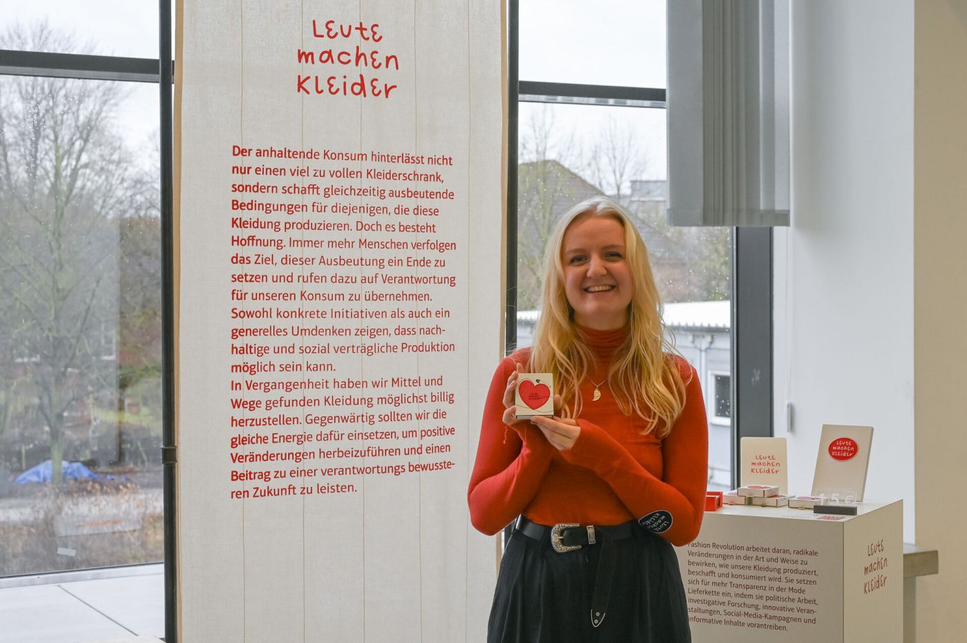  Eine Frau zeigt an einem Ausstellungsstand eine Karte, auf der in einem Herz die Worte "Leute machen Kleider" zu lesen sind.