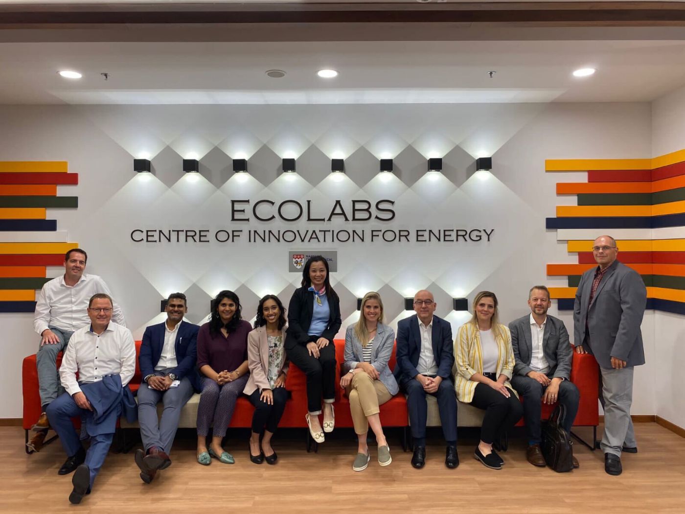 Sechs Männer und fünf Frauen sitzen auf einem Sofa im Ecolabs Centre Of Innovation For Energy.