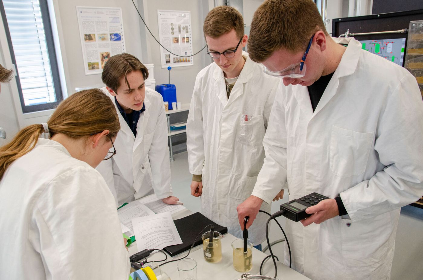 Drei Männer und eine Frau in Laborkitteln untersuchen eine Wasserprobe. (Foto: FH Münster/Frederik Tebbe)