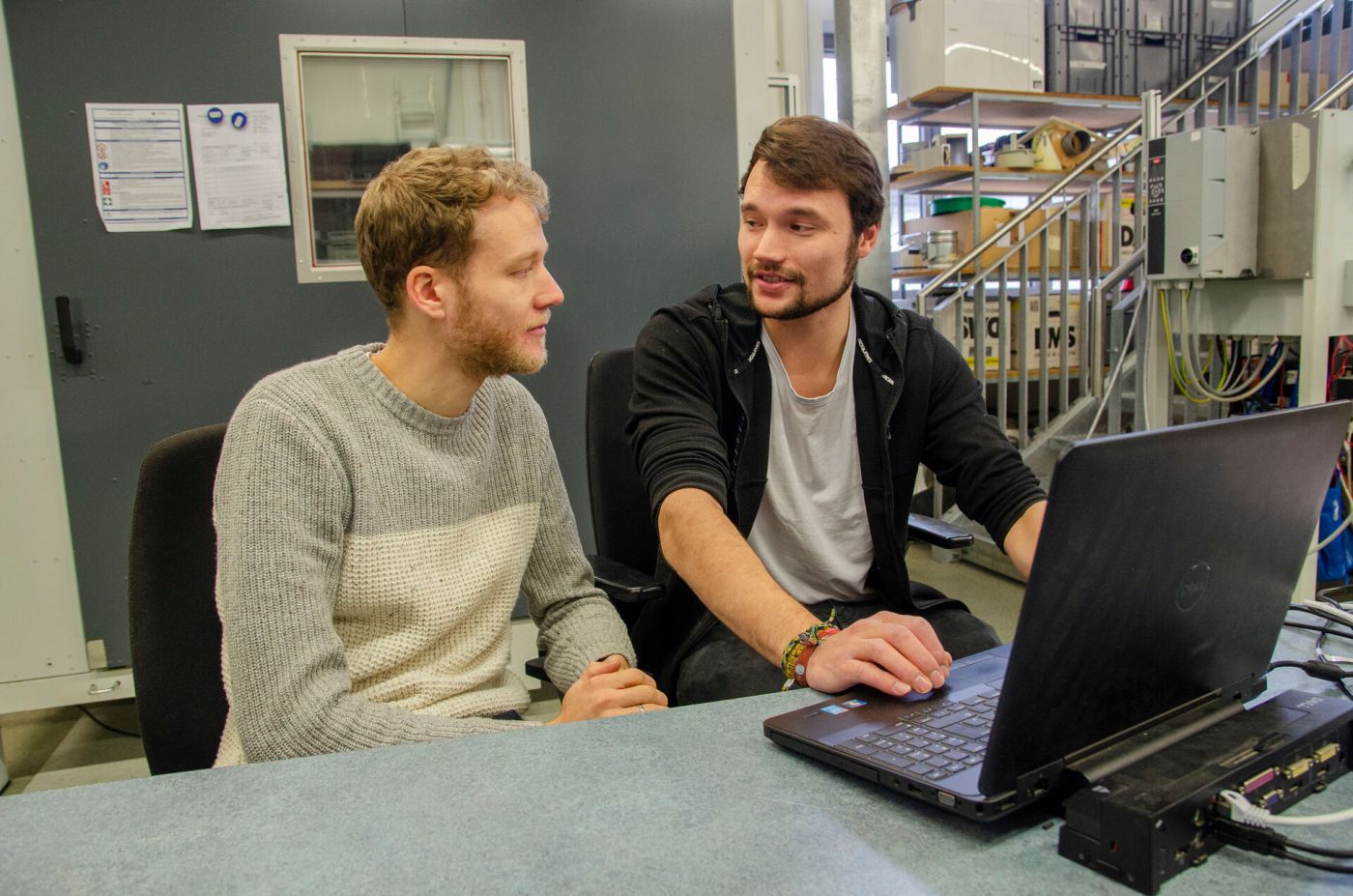 Zwei Männer arbeiten an einem Laptop und unterhalten sich miteinander. 