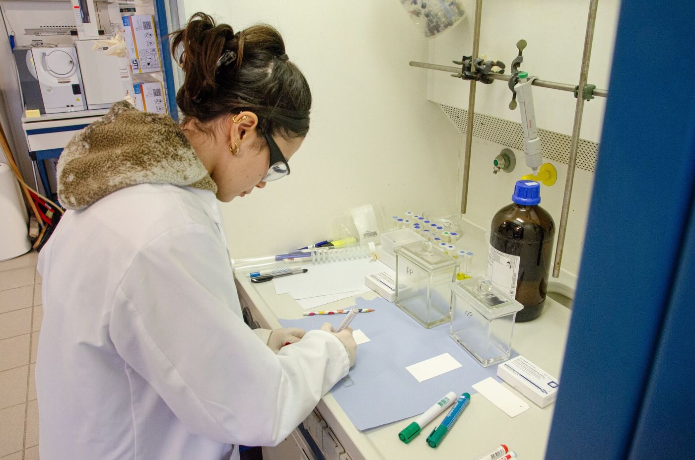 Ein junge Frau mit Kittel und Schutzbrille arbeitet in einem chemischen Labor. (Foto: FH Münster/Frederik Tebbe)