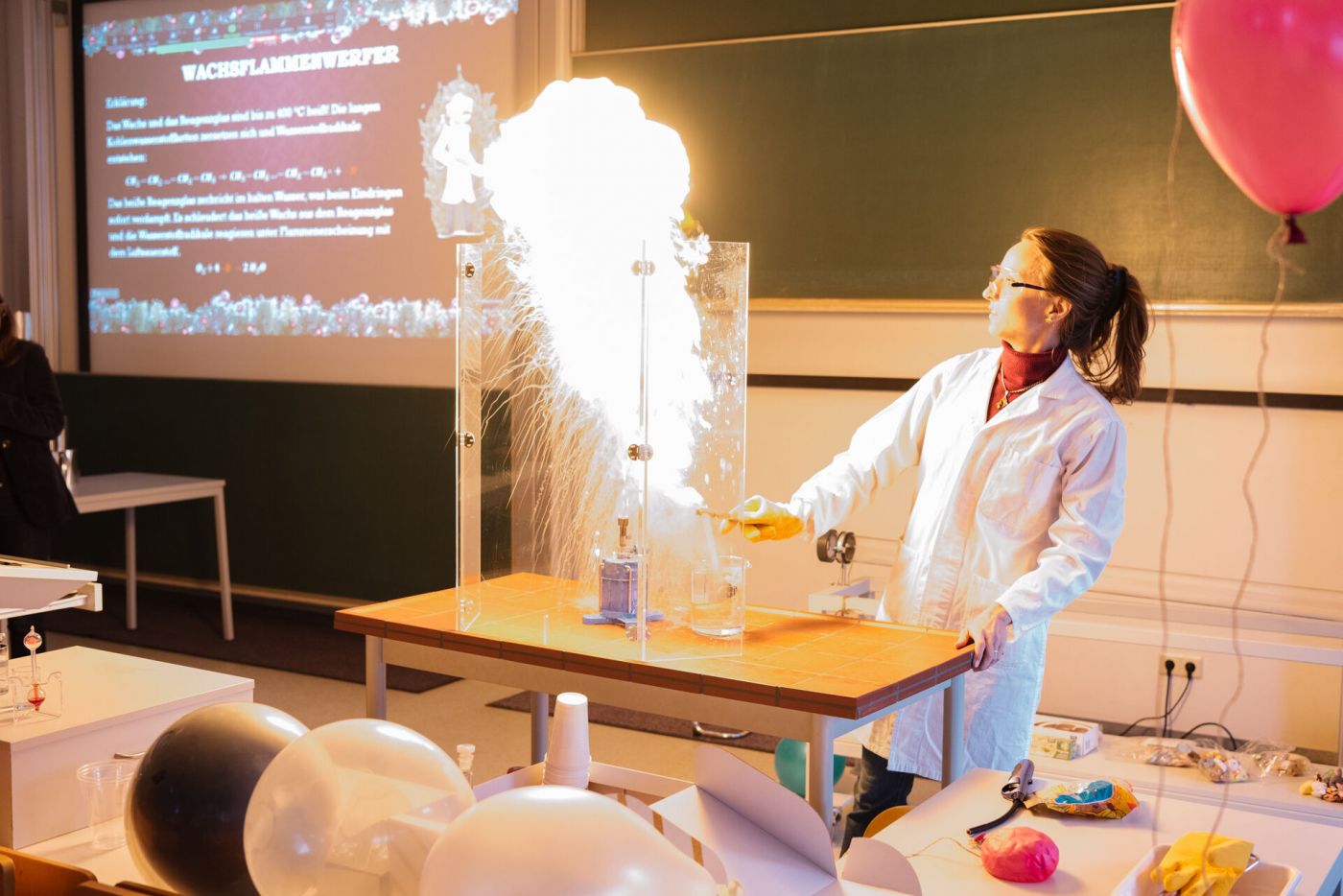 Eine Professorin führt ein Experiment durch, bei dem eine Feuerfontäne aus einem Stück Wachs hinausplatzt.