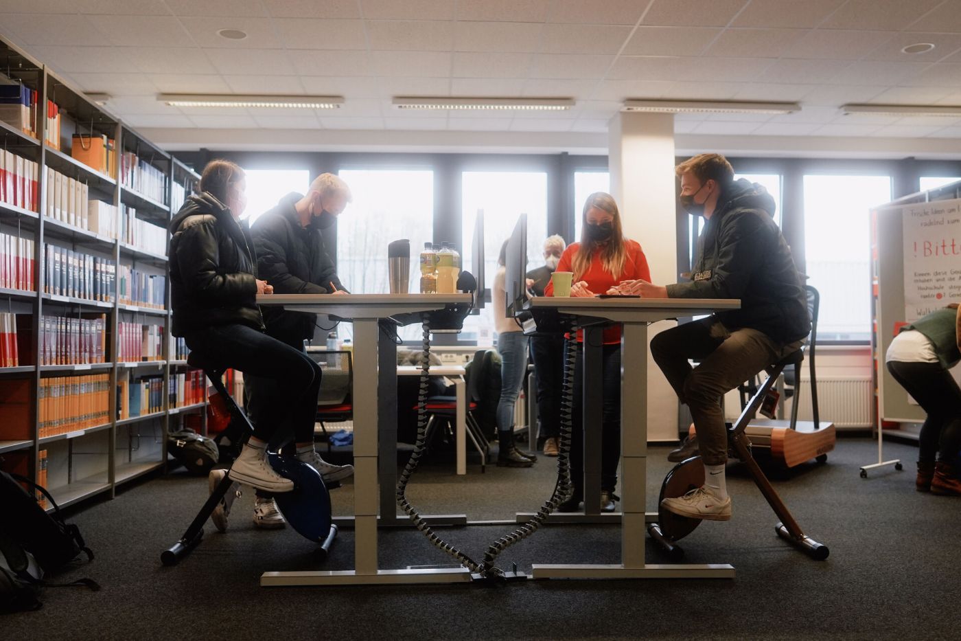 Studierende probieren die Deskbikes aus: Trimmdichräder, auf denen sie fahren können, während sie am Schreibtisch arbeiten.