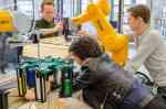 Zwei Männer und eine Frau arbeiten an einem Roboterarm, der Dominosteine aufstellt. (Foto: FH Münster/Frederik Tebbe)