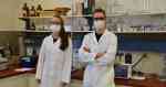Eine Frau und ein Mann stehen in einem Labor. Sie tragen Laborkittel, Schutzbrillen und OP-Masken.