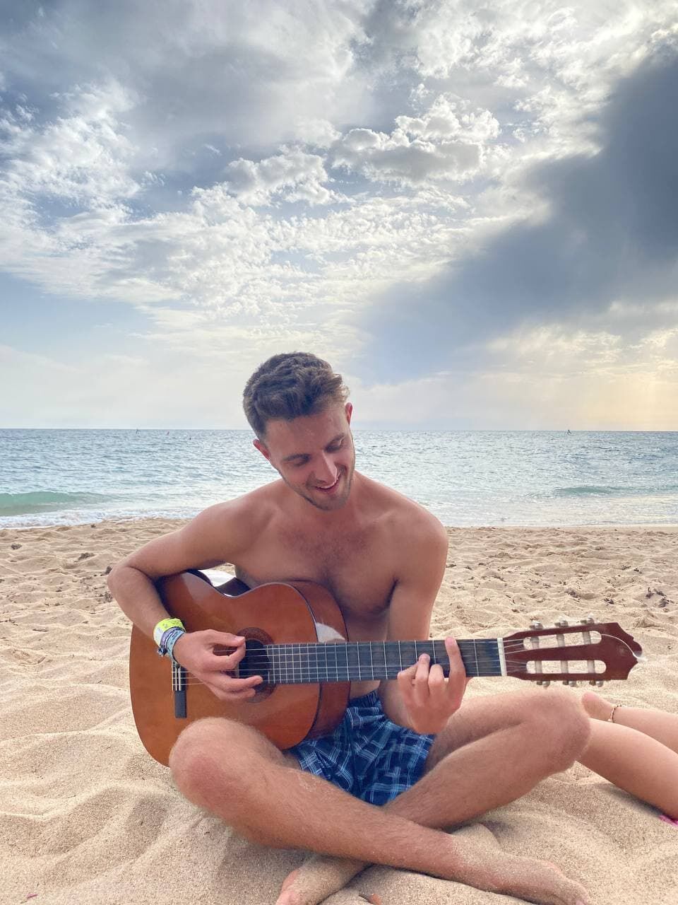 Sebastian sitzt am Strand und spielt Gitarre.