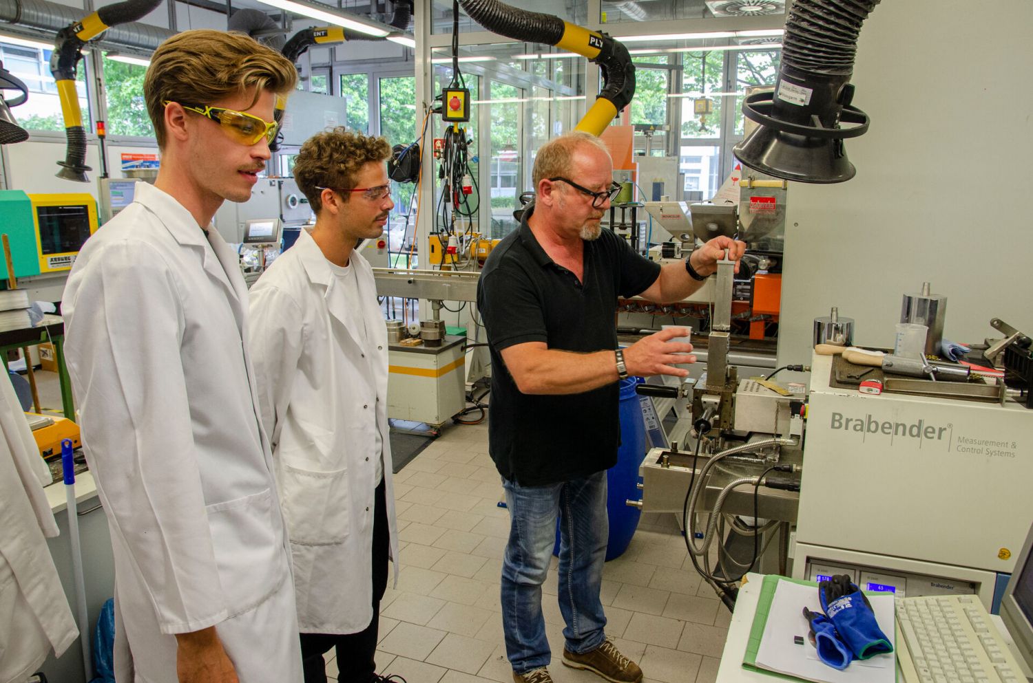 Mit der Unterstützung von Martin Althoff (r.) pressen und verkneten die Studenten Bagasse und ein Biopolymer miteinander, um dies anschließend in der Spritzgießmaschine weiterzuverarbeiten. 