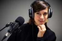 Eine Frau mit Kopfhörern vor einem Mikrofon.