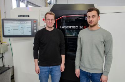 Zwei Männer stehen vor einem Metall 3D-Drucker.